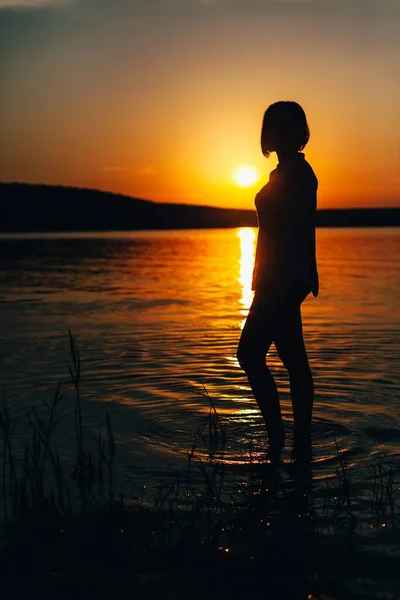 Молодая девушка стоит на пляже на фоне заката . — стоковое фото