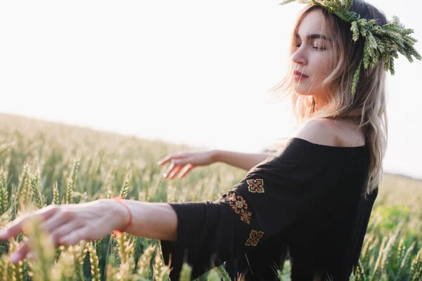 Junges, schlankes Mädchen in einem Kranz aus Weizenähren bei Sonnenuntergang auf einem Feld — Stockfoto