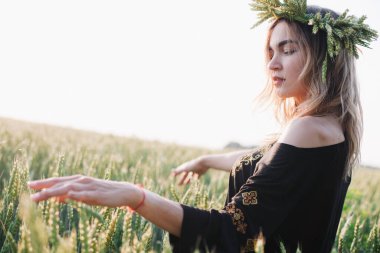 Gün batımında bir tarlada buğday çelengi içinde genç, narin bir kız.