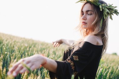 Gün batımında bir tarlada buğday çelengi içinde genç, narin bir kız.