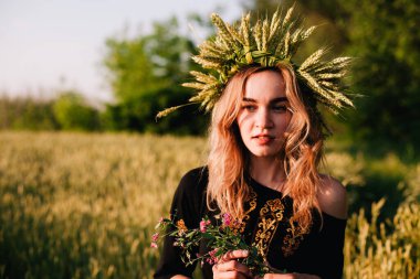 Gün batımında bir tarlada buğday çelengi içinde genç, narin bir kız.