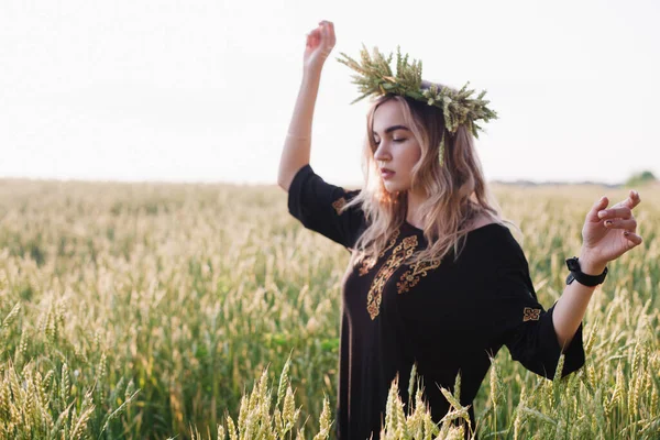 Menina jovem, esbelta em uma grinalda de espigas de trigo ao pôr do sol em um campo — Fotografia de Stock