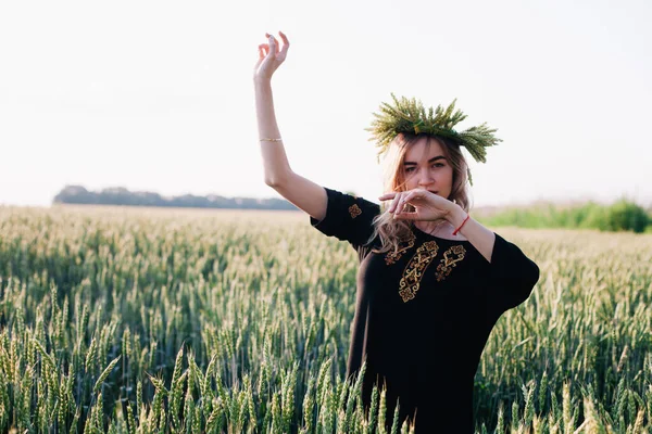 Menina jovem, esbelta em uma grinalda de espigas de trigo ao pôr do sol em um campo — Fotografia de Stock