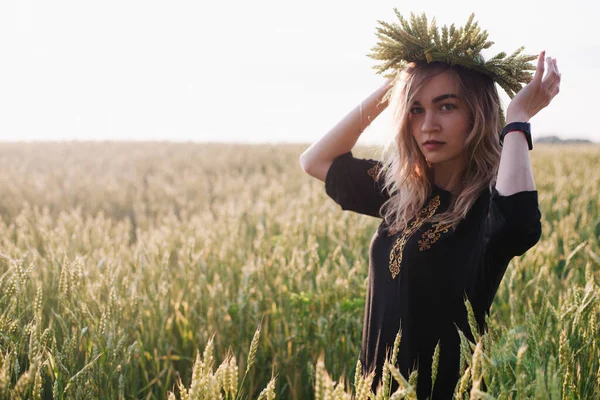 Menina jovem, esbelta em uma grinalda de espigas de trigo ao pôr do sol em um campo — Fotografia de Stock