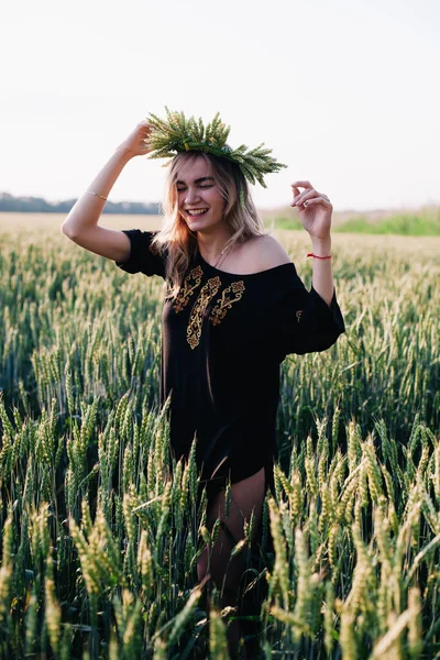 Jeune fille mince dans une couronne d'oreilles de blé au coucher du soleil dans un champ — Photo