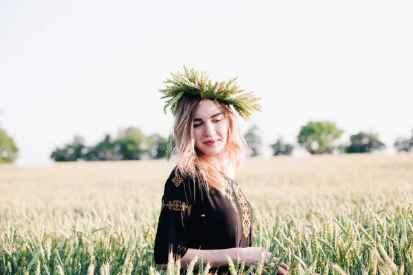 Menina jovem, esbelta em uma grinalda de espigas de trigo ao pôr do sol em um campo — Fotografia de Stock