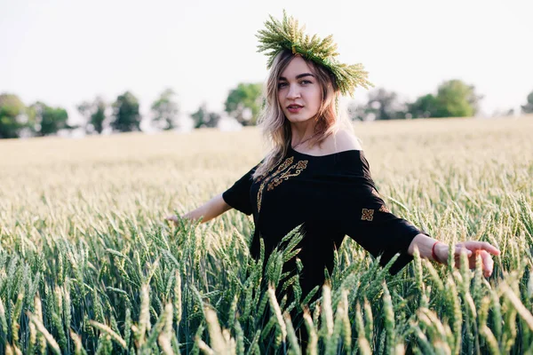 Menina jovem, esbelta em uma grinalda de espigas de trigo ao pôr do sol em um campo — Fotografia de Stock