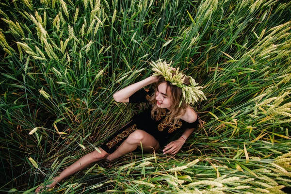En ung, smal flicka i broderi ligger i veteöron på ett fält — Stockfoto