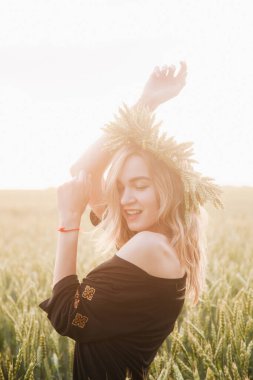 Gün batımında bir tarlada buğday çelengi içinde genç, narin bir kız.