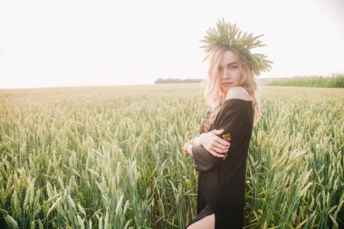 Gün batımında bir tarlada buğday çelengi içinde genç, narin bir kız.