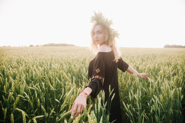 Menina jovem, esbelta em uma grinalda de espigas de trigo ao pôr do sol em um campo — Fotografia de Stock