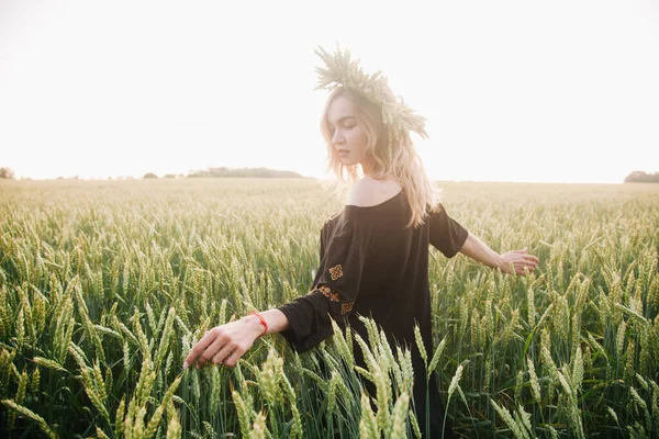 Menina jovem, esbelta em uma grinalda de espigas de trigo ao pôr do sol em um campo — Fotografia de Stock