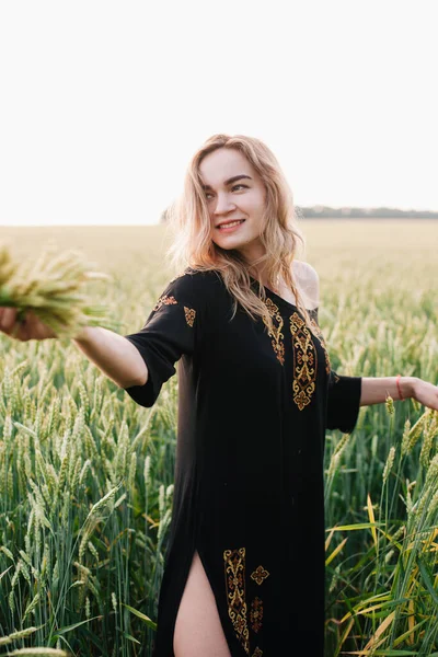Jovem, vestido bordado menina esbelta em um grande campo de trigo ao pôr do sol — Fotografia de Stock