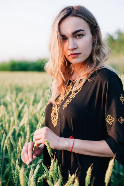 Jovem, vestido bordado menina esbelta em um grande campo de trigo ao pôr do sol — Fotografia de Stock