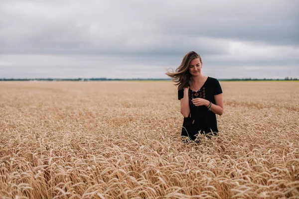 Menina bonita, esbelta em um campo de trigo contra o céu de chuva — Fotografia de Stock