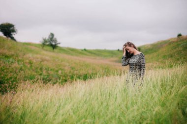Üzerinde kır çiçekleri olan çayırlık bir elbise içinde güzel, ince bir kız.
