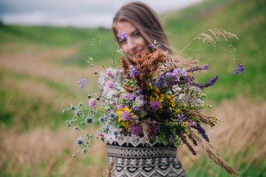 Üzerinde kır çiçekleri olan çayırlık bir elbise içinde güzel, ince bir kız.