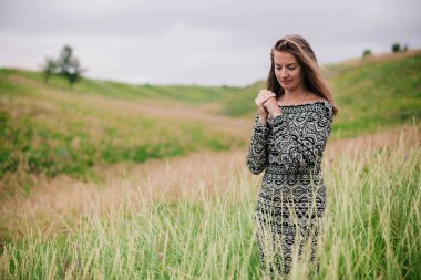 Üzerinde kır çiçekleri olan çayırlık bir elbise içinde güzel, ince bir kız.