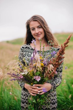Üzerinde kır çiçekleri olan çayırlık bir elbise içinde güzel, ince bir kız.