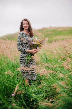 Üzerinde kır çiçekleri olan çayırlık bir elbise içinde güzel, ince bir kız.