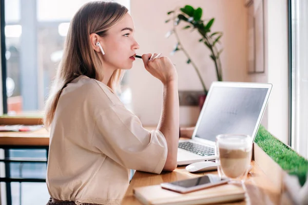 Młoda dziewczyna pracuje w laptopie w kawiarni i pije cappuccino. — Zdjęcie stockowe