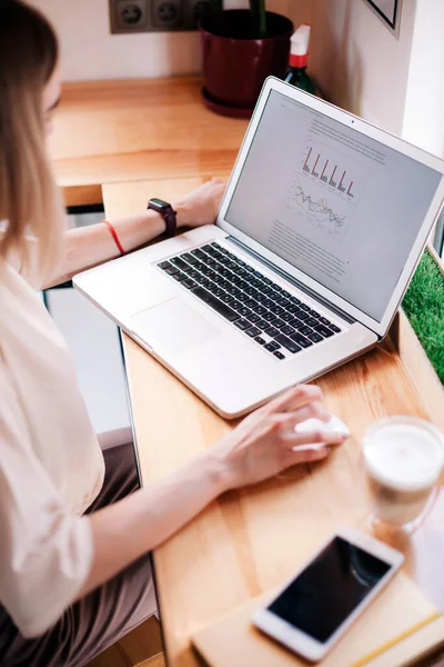 En ung flicka arbetar på en bärbar dator på ett café och dricker cappuccino. — Stockfoto