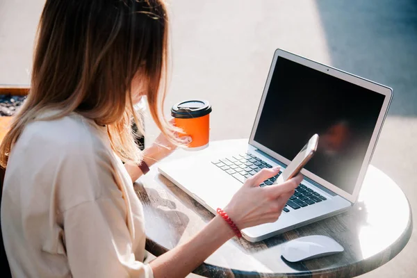 Yazın oyun bahçesindeki bir kafede laptopun arkasında çalışan ve tek kullanımlık bir bardaktan kahve içen genç bir kız. 
