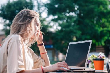 Yazın oyun bahçesindeki bir kafede laptopun arkasında çalışan ve tek kullanımlık bir bardaktan kahve içen genç bir kız. 