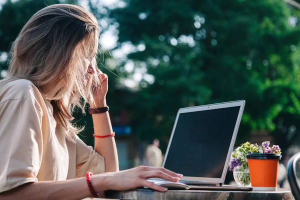 Yazın oyun bahçesindeki bir kafede laptopun arkasında çalışan ve tek kullanımlık bir bardaktan kahve içen genç bir kız. 