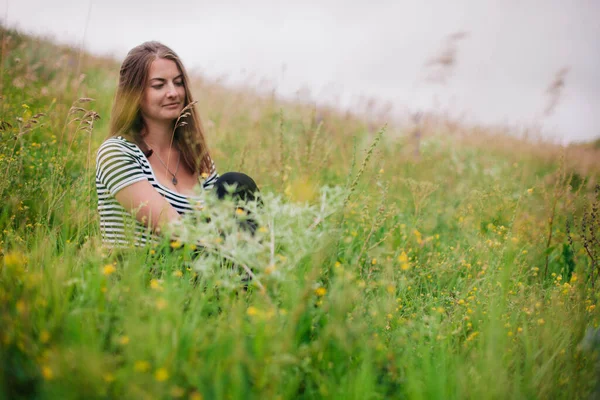 Schöne Mädchen in einem schwarzen langen Rock und gestreiftem T-Shirt sitzt am Hang einer grünen Wiese — Stockfoto