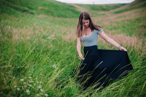 Beautiful girl in a black long skirt and striped T-shirt walks in green hole — Stock Photo, Image