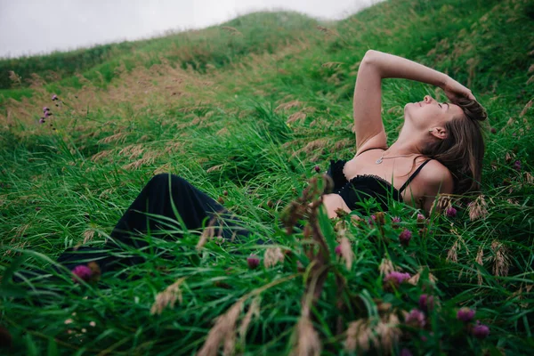 Menina bonita em sutiã preto e saia longa encontra-se na grama — Fotografia de Stock
