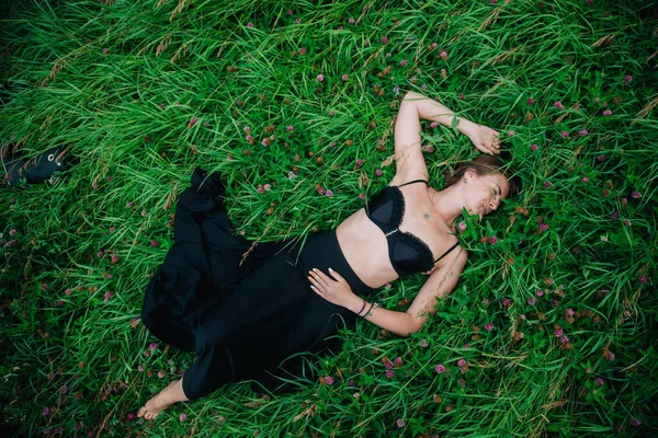 Piękna dziewczyna w czarnym staniku i długiej spódnicy leży w trawie — Zdjęcie stockowe