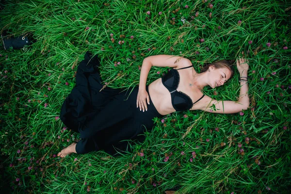 Siyah sütyenli ve uzun etekli güzel kız çimenlerde yatıyor. — Stok fotoğraf