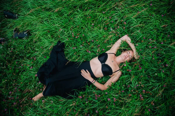 Hermosa chica en sujetador negro y falda larga se encuentra en la hierba — Foto de Stock