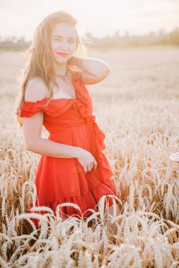 Kırmızı elbiseli ve çizgili şapkalı güzel kız buğday tarlasında poz veriyor.