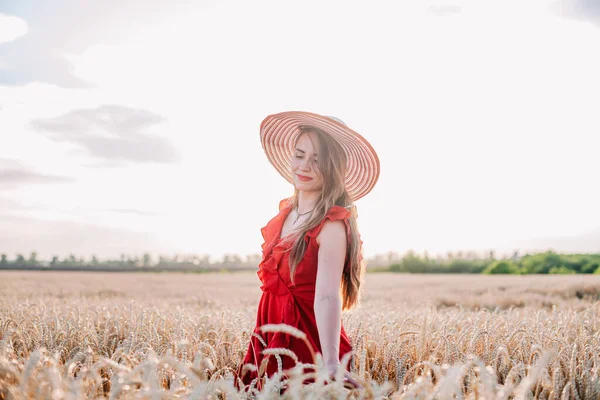 美しいです女の子で赤いドレスと縞模様の帽子ポージングで小麦フィールド — ストック写真