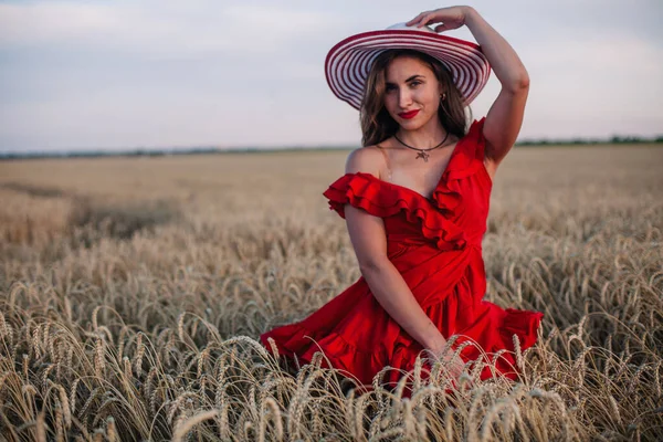 Belle fille en robe rouge et chapeau rayé posant dans un champ de blé — Photo