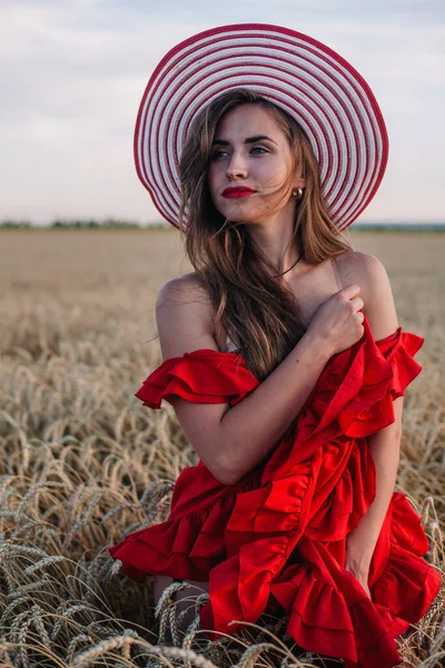 Belle fille en robe rouge et chapeau rayé posant dans un champ de blé — Photo