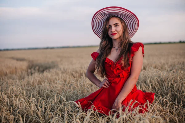 Hermosa chica en vestido rojo y sombrero a rayas posando en un campo de trigo — Foto de Stock