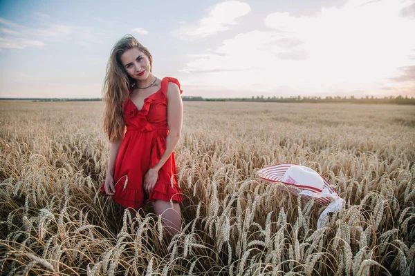 Piękna dziewczyna w czerwonej sukience i kapelusz w paski pozowanie na polu pszenicy — Zdjęcie stockowe