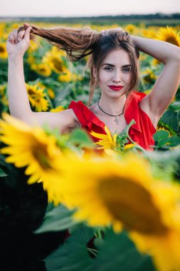 Kırmızı elbiseli, ince, genç bir kız ayçiçeği tarlasında poz veriyor.
