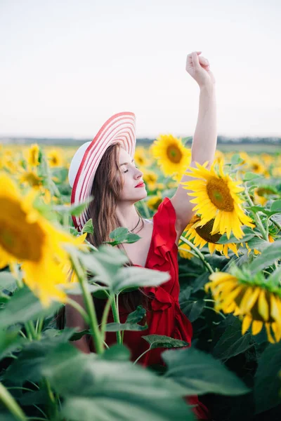 Une jeune fille mince dans une robe rouge pose dans un champ de tournesols — Photo