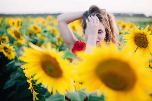 Una joven esbelta con un vestido rojo posa en un campo de girasoles —  Fotos de Stock