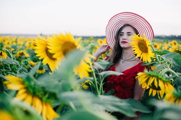 Una joven esbelta con un vestido rojo posa en un campo de girasoles — Foto de Stock