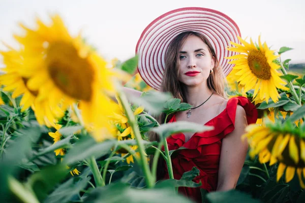 Молода струнка дівчина в червоній сукні позує в полі соняшників — стокове фото