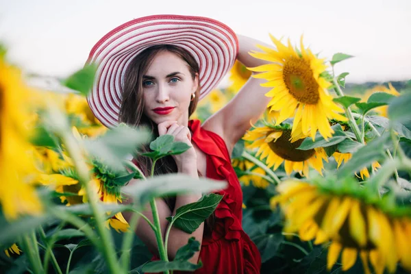 Una joven esbelta con un vestido rojo posa en un campo de girasoles — Foto de Stock