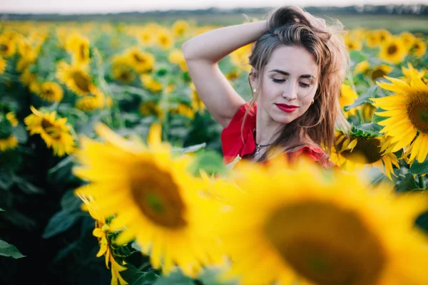 Una giovane ragazza snella con un vestito rosso posa in un campo di girasoli — Foto Stock