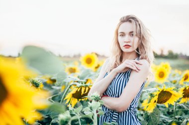 Tişörtlü genç bir kız ayçiçeklerinin içinde duruyor.