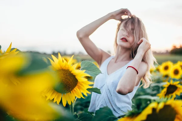 白いTシャツを着た若い女性がひまわり畑の夕日にポーズをとっている — ストック写真